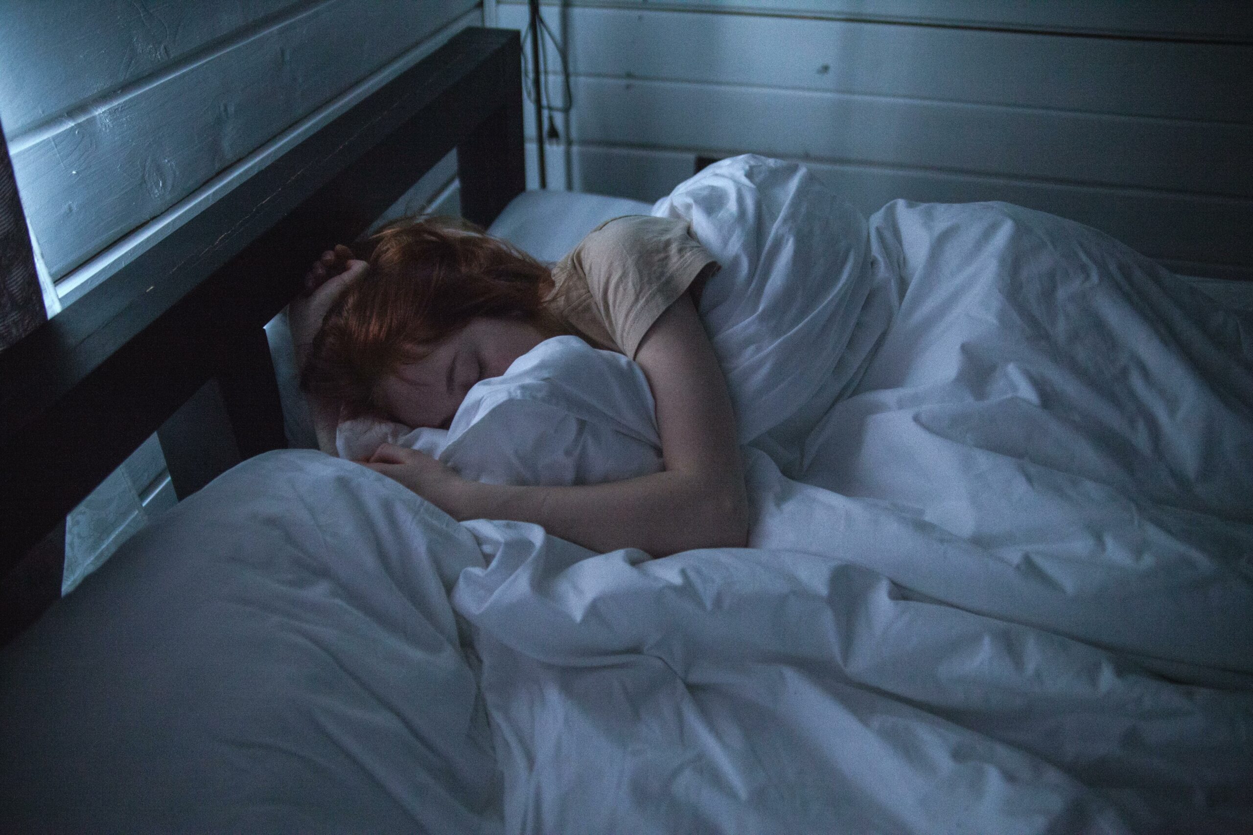 Person sleeping in bed, surrounded by white bedding, illustrating the symptoms of excessive daytime sleepiness associated with idiopathic hypersomnia (IH).